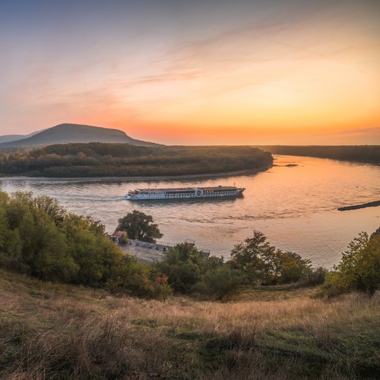 Panoramablick vom Ufer auf die Donau bei Bratislava während des Sonnenuntergangs. Ein Flussschiff fährt vorbei.