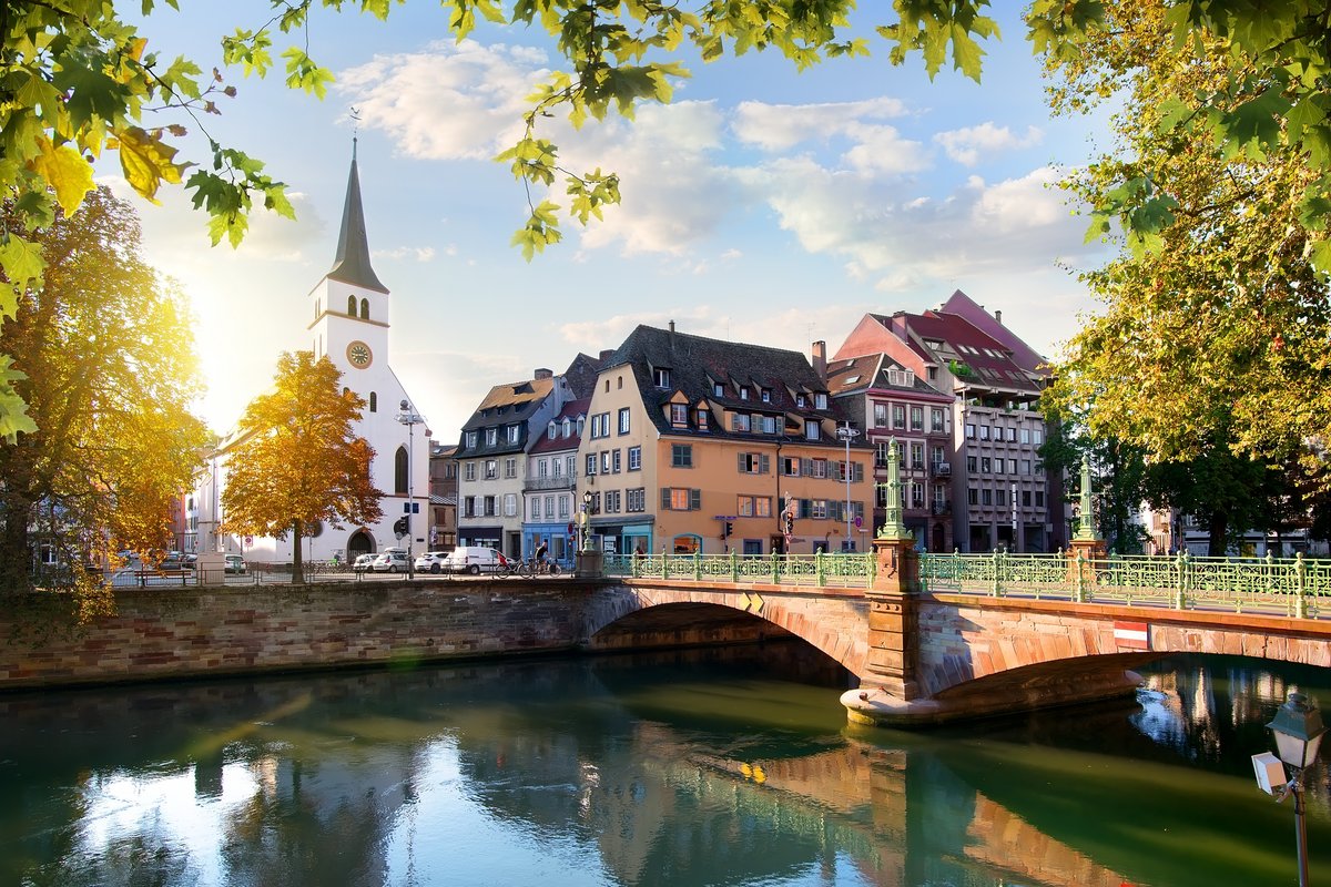 Old town of Strasbourg with half-timbered houses and canals, surrounded by green trees, under a blue sky.