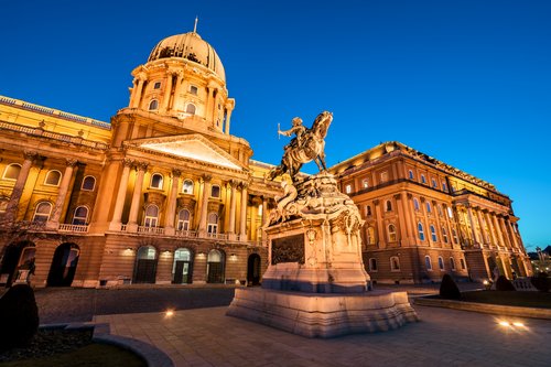 Beleuchtetes Budaer Schloss mit Kuppel und Reiterstatue bei Abenddämmerung in Budapest