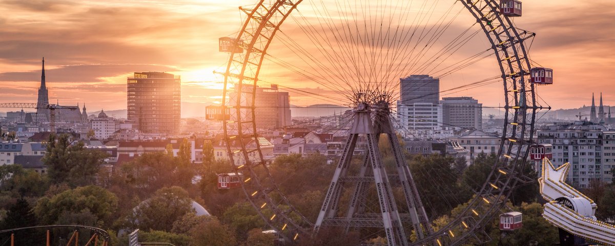 View of downtown Vienna with the Vienna Prater and a large ferris wheel in the foreground, at sunset.