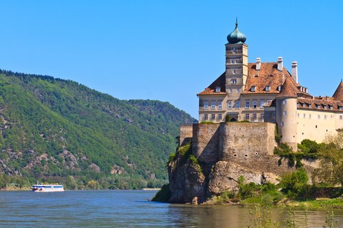 Schloss Schönbühel thront majestätisch auf einem Hügel über der Donau, umgeben von üppigem Grün und strahlend blauem Himmel.