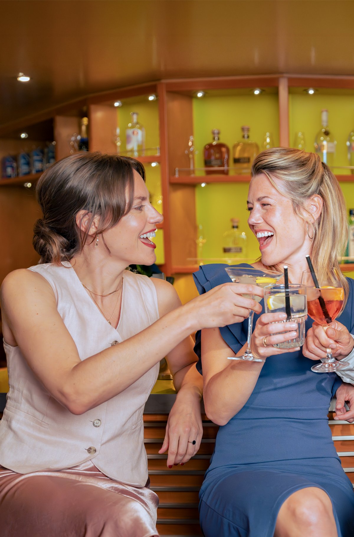 Gäste stoßen mit bunten Cocktails und Drinks an einer modern beleuchteten Bar, auf einem A-ROSA Flusskreuzfahrtschiff an.