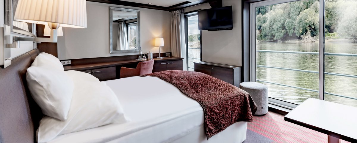 The junior suite on board the A-ROSA CLEA with double bed, seating area, floor-to-ceiling windows, and juliette balcony.