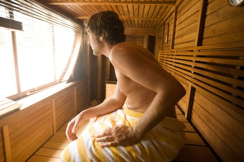 A man relaxing in the modern sauna with wooden benches and a large window offering a view of the surrounding nature.