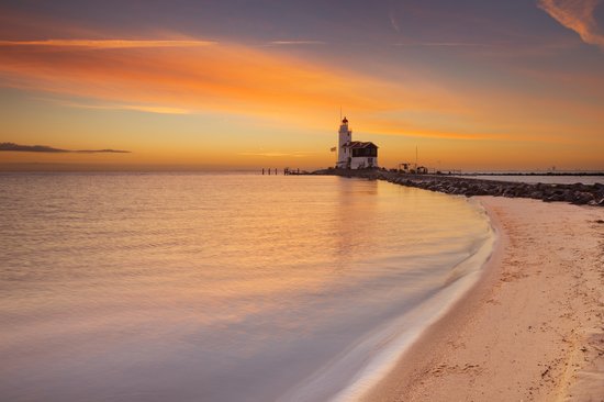 Leuchtturm am Ende eines Steinwegs bei Sonnenuntergang mit orangefarbenem Himmel und ruhigem Meer