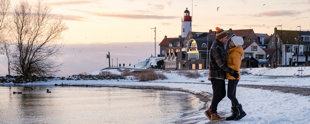 Winter landscape at the IJsselmeer with a snow-covered shore and a winter-dressed couple on the shore embracing each other.