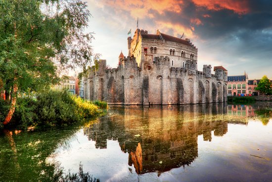 Burg Gravensteen in Gent, Belgien, mit mittelalterlicher Architektur und Türmen, umgeben von Wassergraben und Bäumen.