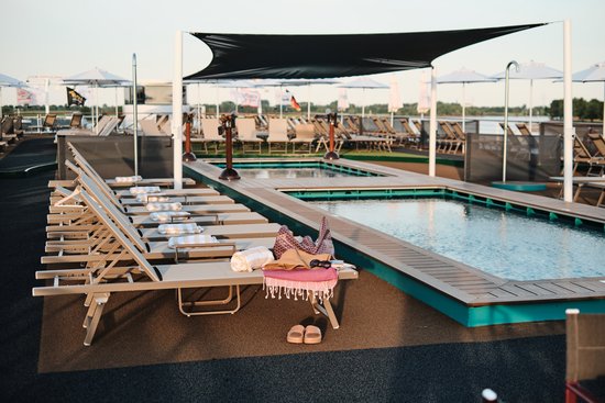 The sun deck of the A-ROSA SENA in daylight with a swimming pool and kids pool as well as numerous deck chairs.