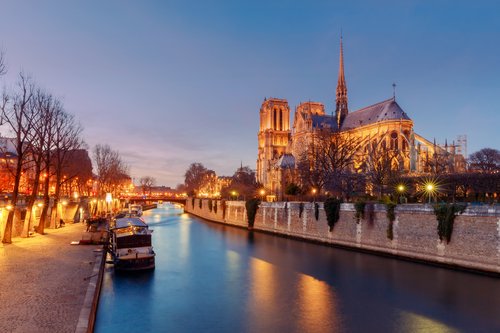 Notre Dame in Paris on the riverbank during dusk. Small boats dock on the river.